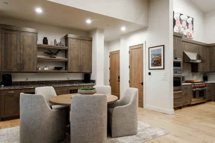 Open-concept space featuring a dining area with a round wood-finish table and upholstered chairs, alongside a kitchen with wood-finish cabinetry, stainless steel appliances, and a range hood