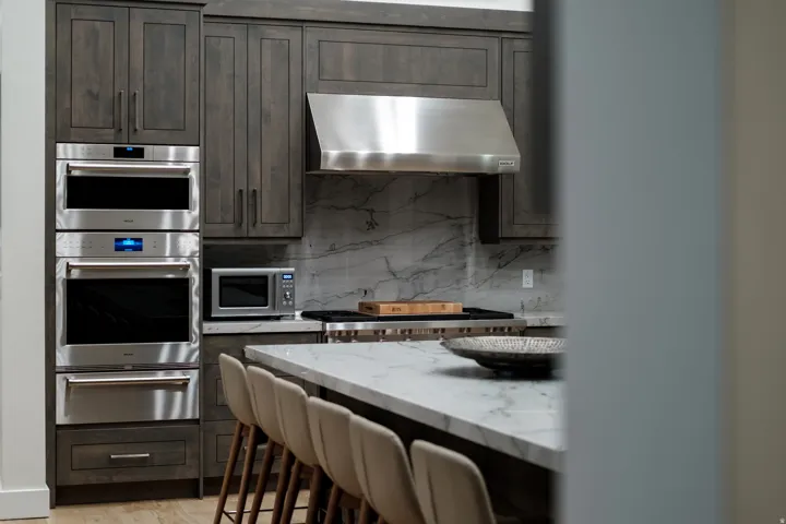 Kitchen featuring dark wood cabinetry, integrated stainless steel appliances, and a polished stone backsplash