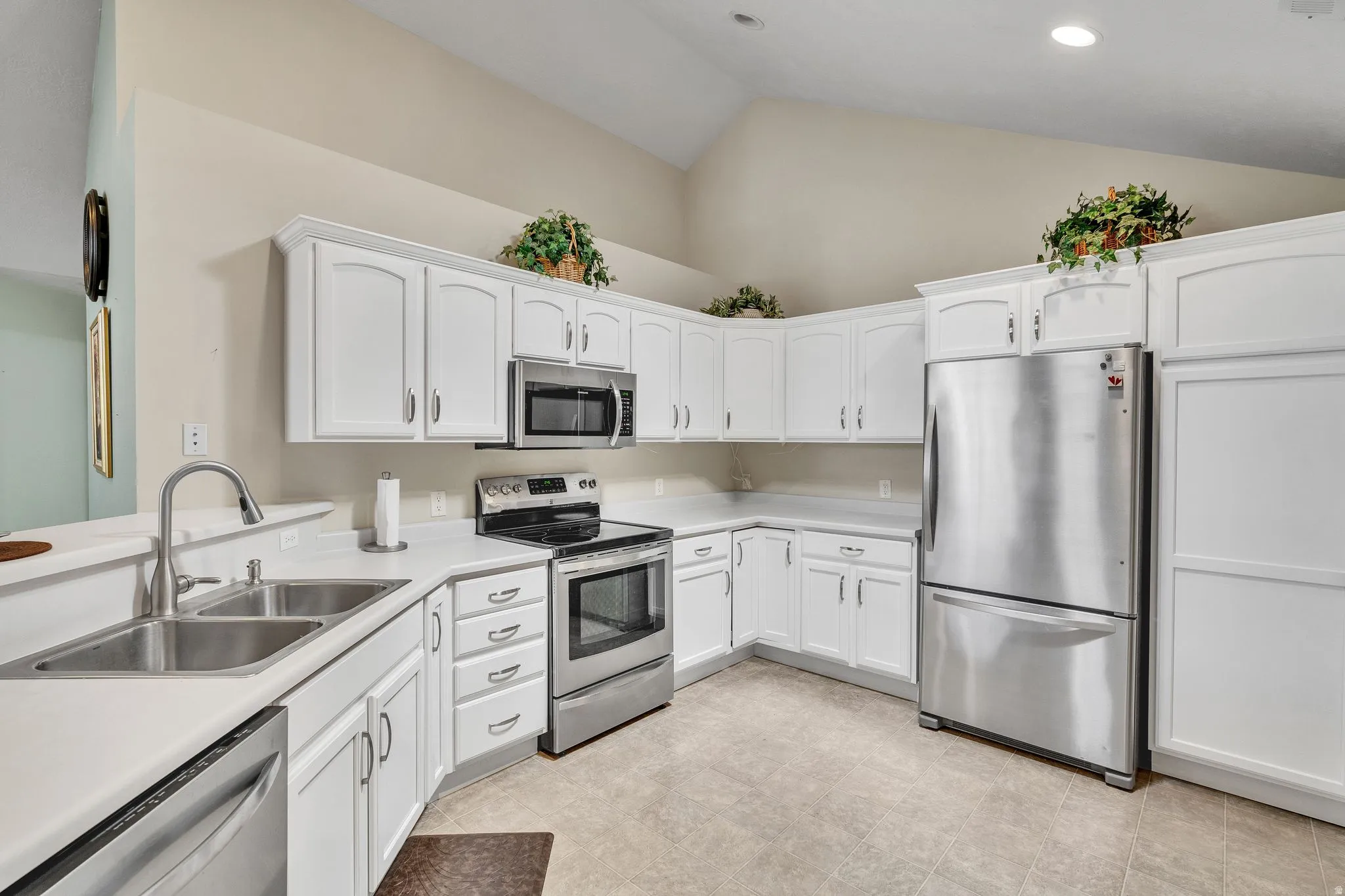 Kitchen featuring white cabinetry, stainless steel appliances, dual basin sink, light-toned countertops, and vaulted ceilings
