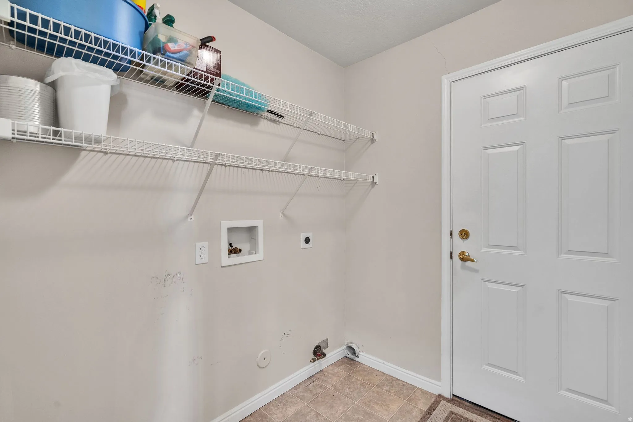 Utility room featuring a paneled white door with brass hardware, two white wire shelving units, and tile flooring