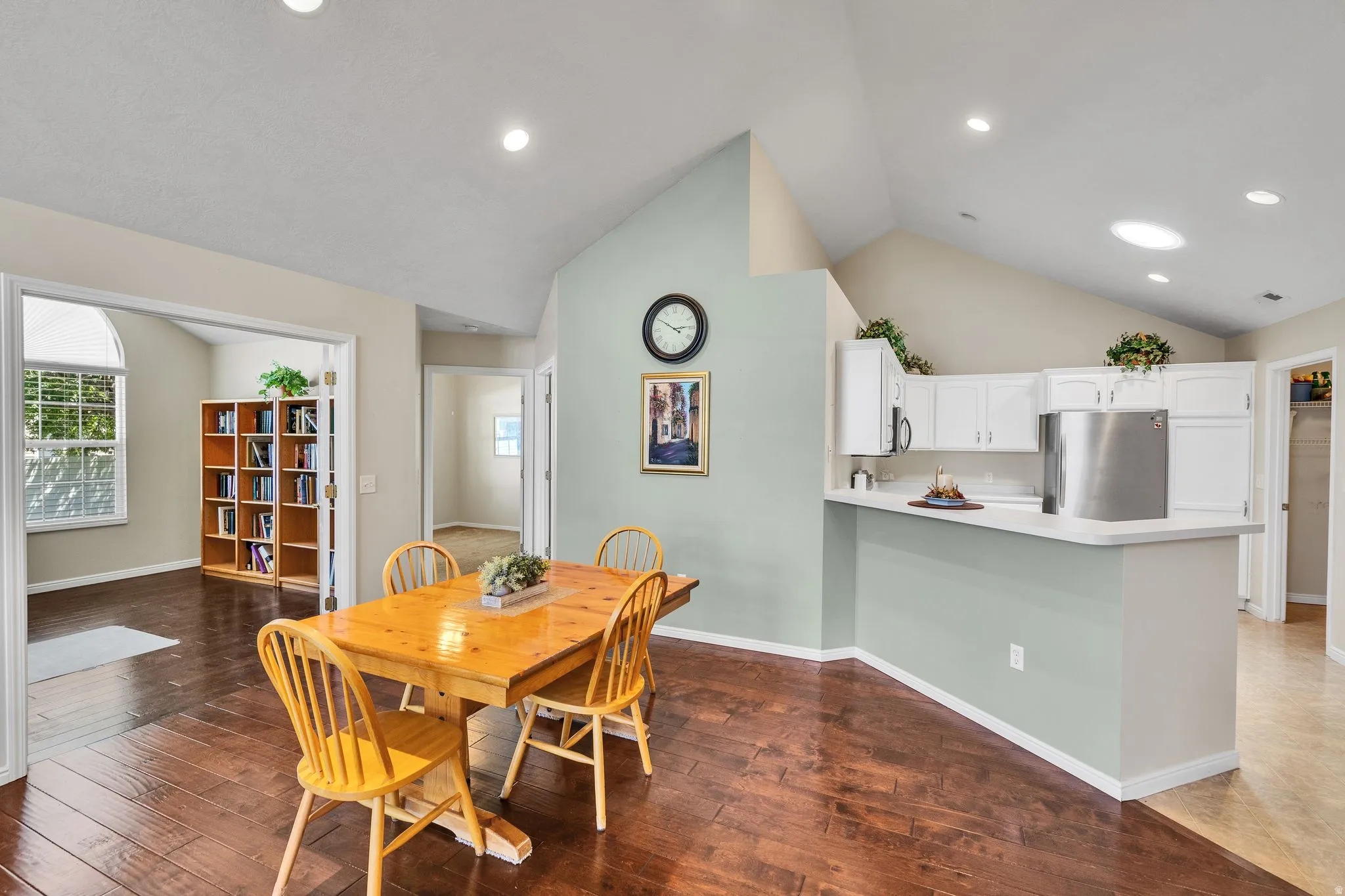 Vaulted ceilings with recessed lighting, wood-finish flooring, white kitchen cabinetry, a kitchen counter bar, and an arched doorway framing a built-in bookcase