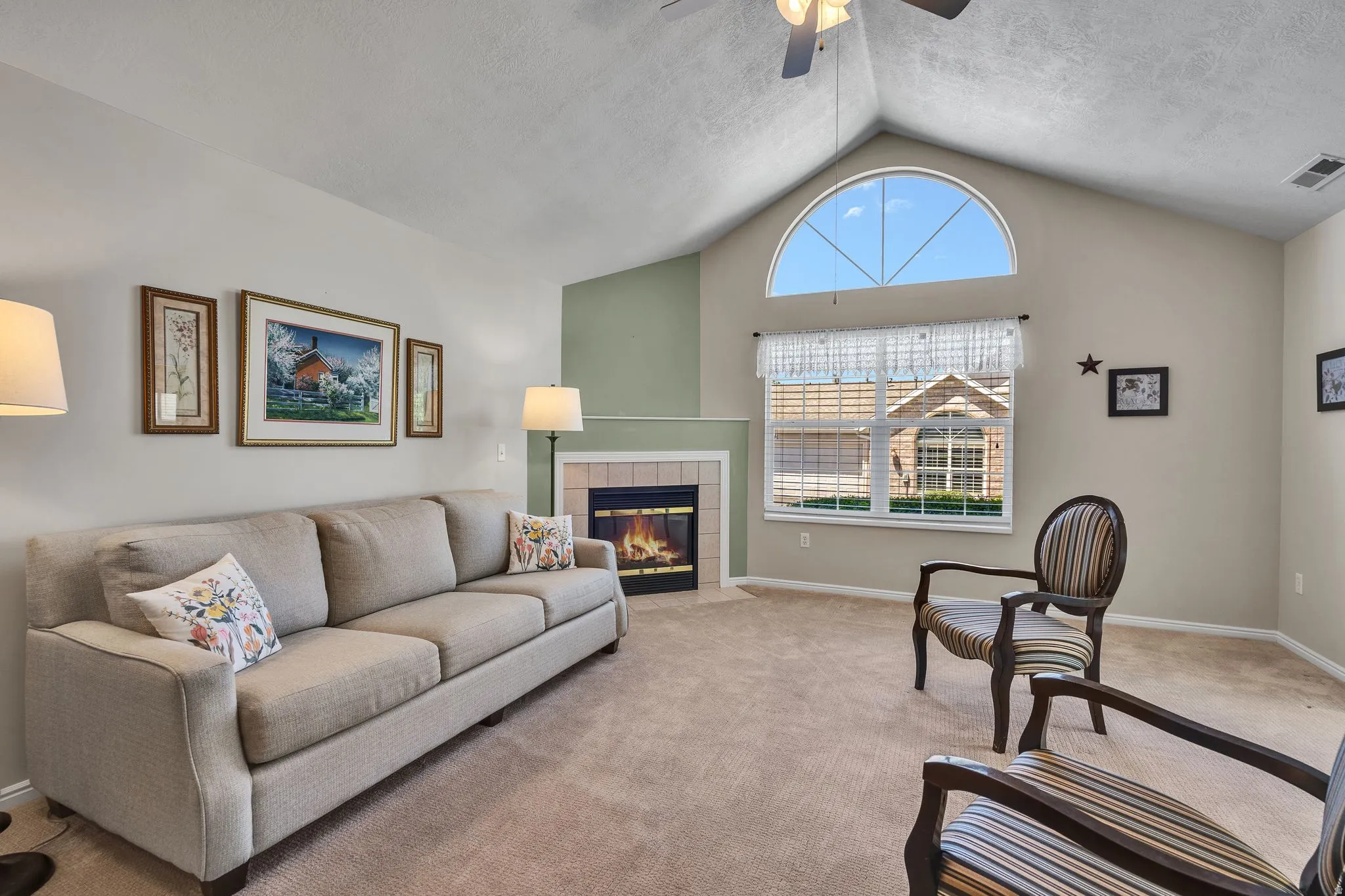 Spacious living area featuring a vaulted ceiling, an arched transom window, a fireplace with a light-colored tile surround, and neutral-toned carpeting