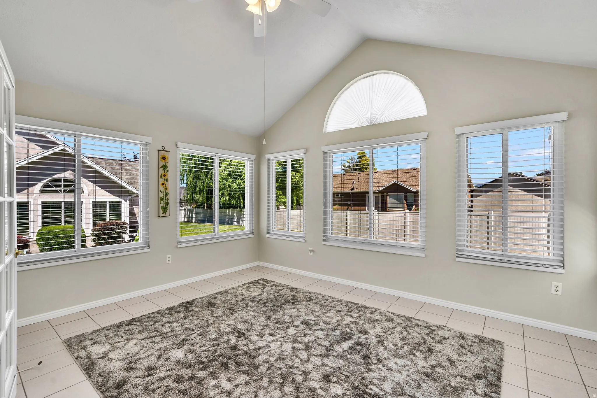 Vaulted ceiling room featuring multiple windows, a half-round transom window, and tile flooring