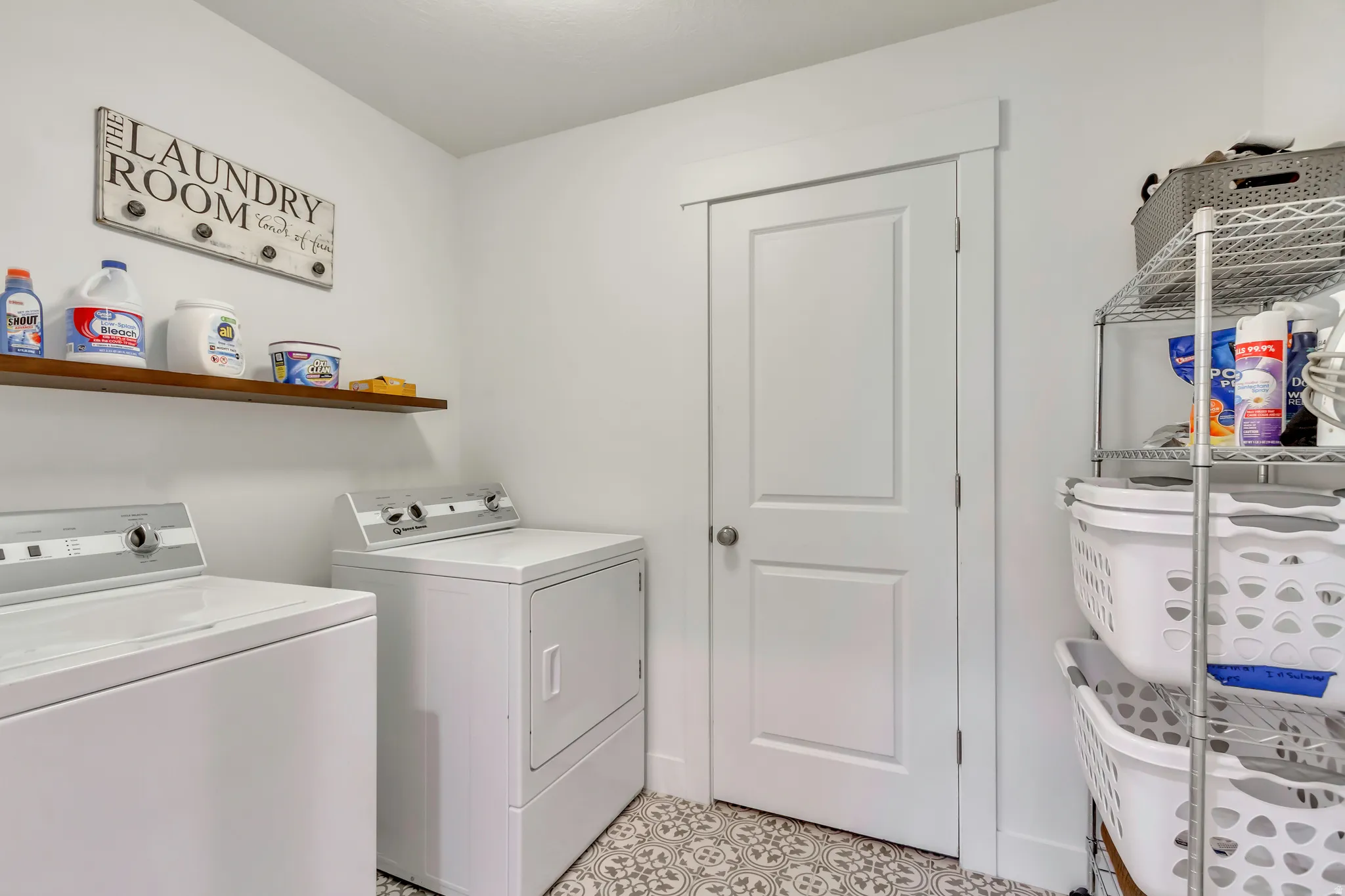 Functional laundry space featuring decorative floor tiling, a floating wood-finish shelf, and a painted door with a contemporary trim