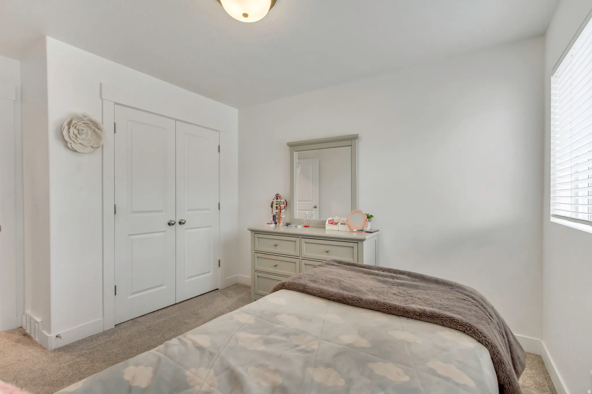 Neutral paint palette, carpeted flooring, window with blinds, and white bi-fold closet doors with chrome hardware