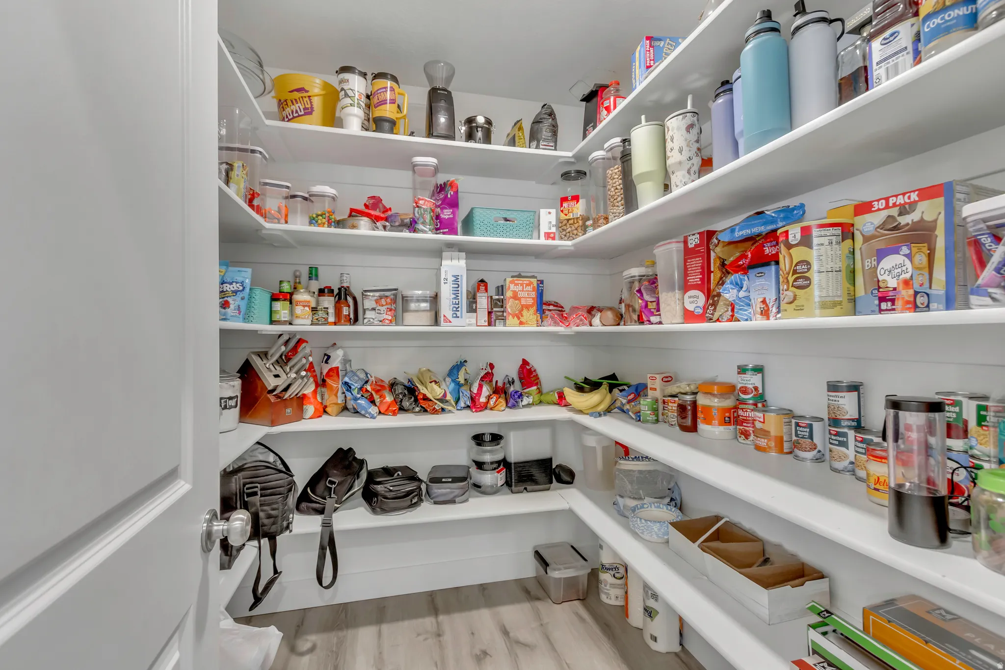 Spacious walk-in pantry featuring white shelving, light wood-finish flooring, and white walls