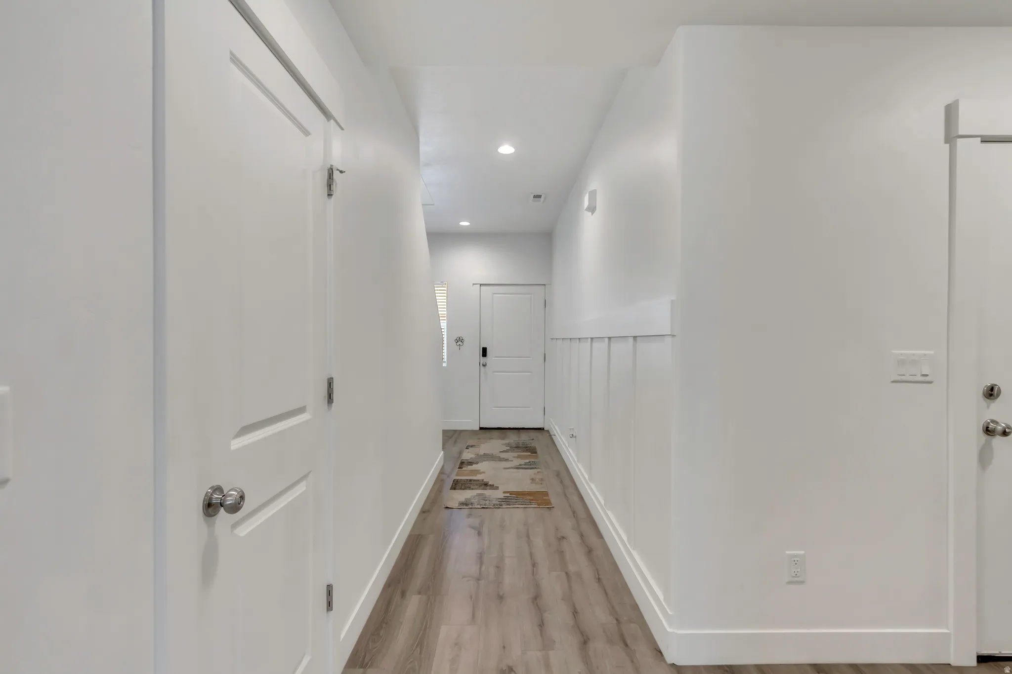 Hallway featuring recessed lighting, wood-finish flooring, white trim, white paneled doors, and board and batten wainscoting