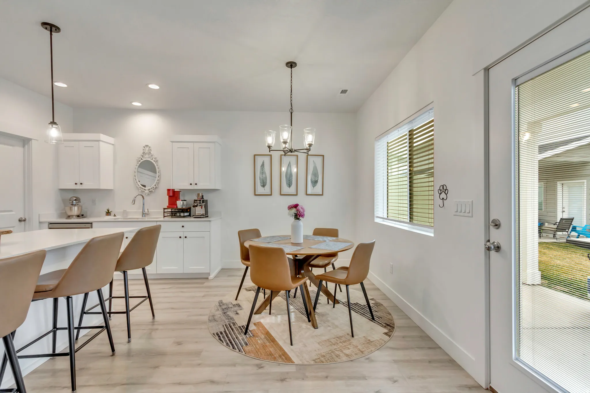 Open-concept living space featuring wood-finish flooring, white cabinetry, a kitchen island with seating, a dining area, and a glass-paneled door leading to an outdoor patio