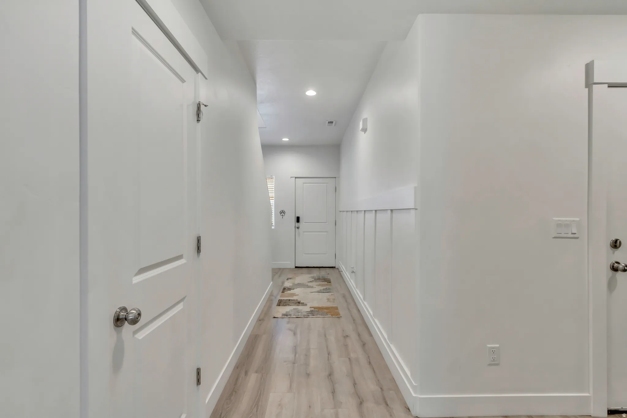 Hallway featuring light wood-finish flooring, recessed lighting, white walls, and wainscoting detail