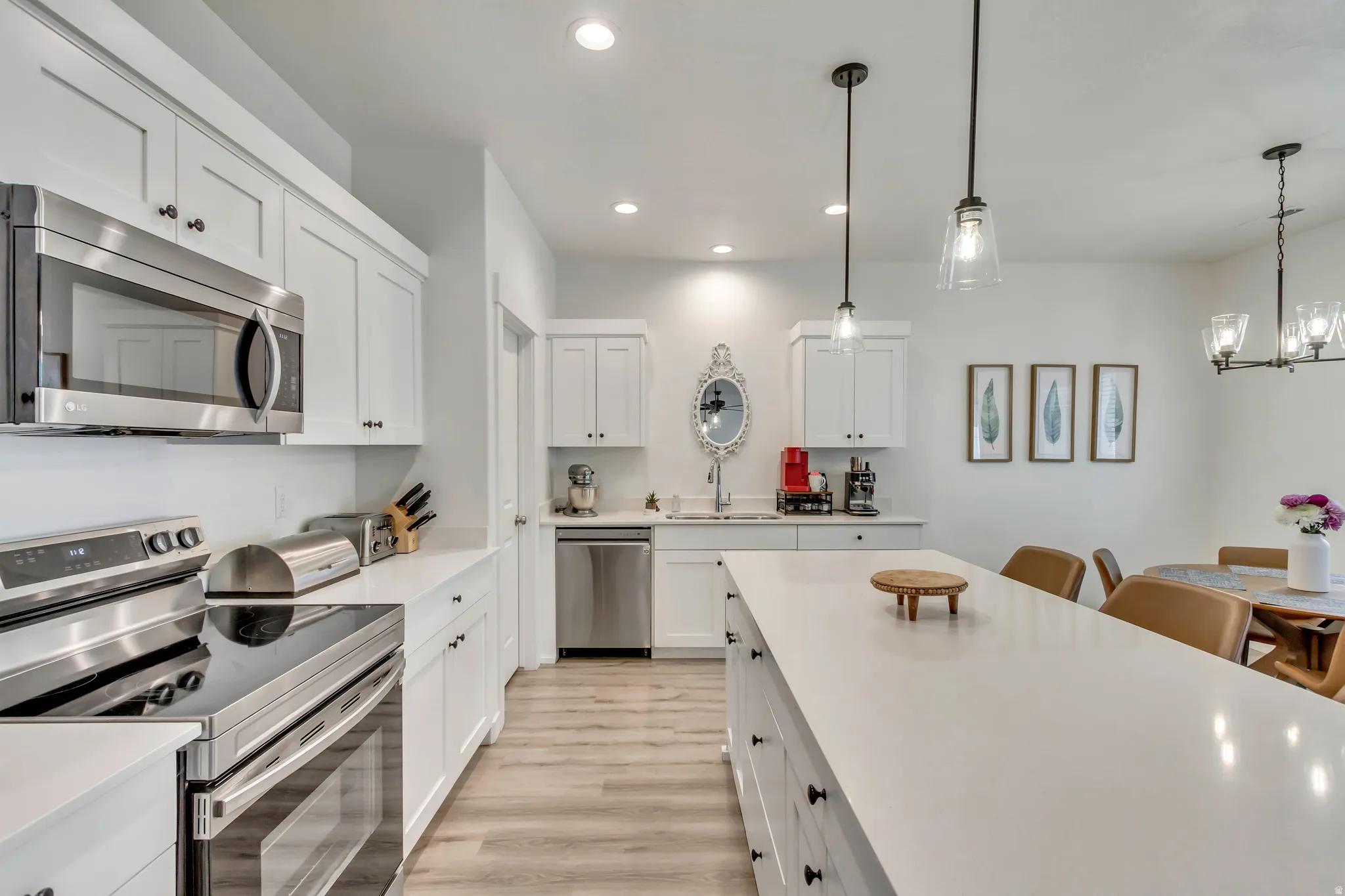 Modern kitchen featuring white shaker cabinetry, stainless steel appliances, light-toned wood-finish flooring, and a large central island with pendant lighting