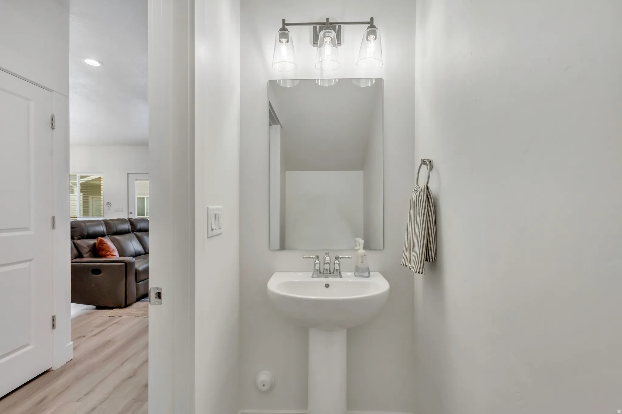 Pedestal sink with chrome faucet, complemented by an overhead three-bulb vanity light fixture