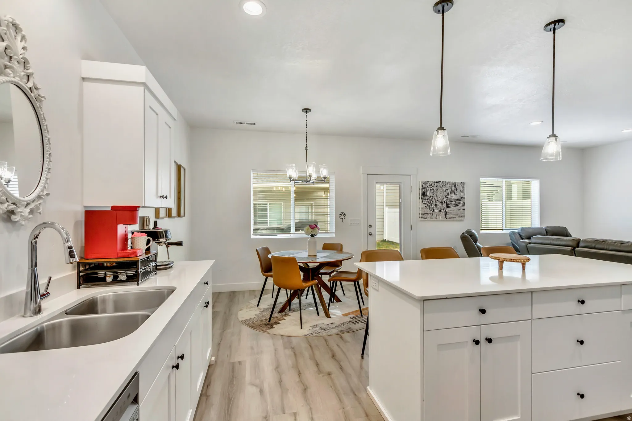 Open-concept kitchen featuring white cabinetry, light-toned wood-finish flooring, a double basin stainless steel sink, and a central island with an integrated countertop
