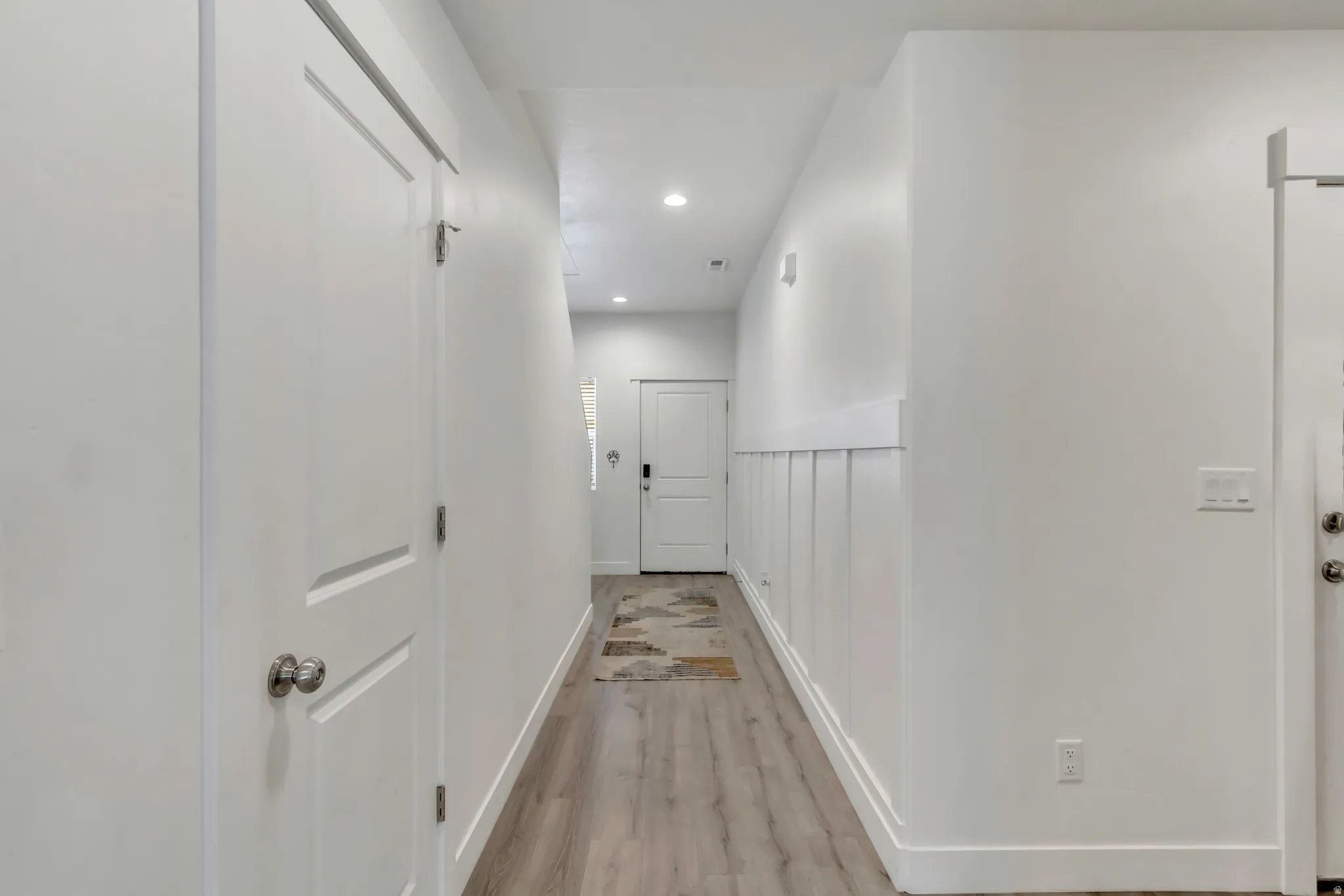 Hallway featuring wood-finish flooring, white panel-style doors, recessed lighting, and wainscoting detail