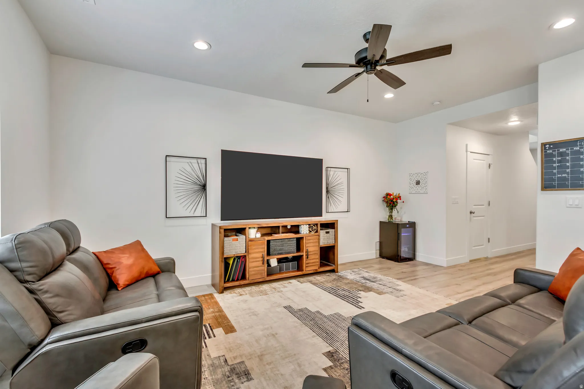 Open-concept living space featuring a ceiling fan, recessed lighting, wood-finish flooring, white baseboards, and a solid white door