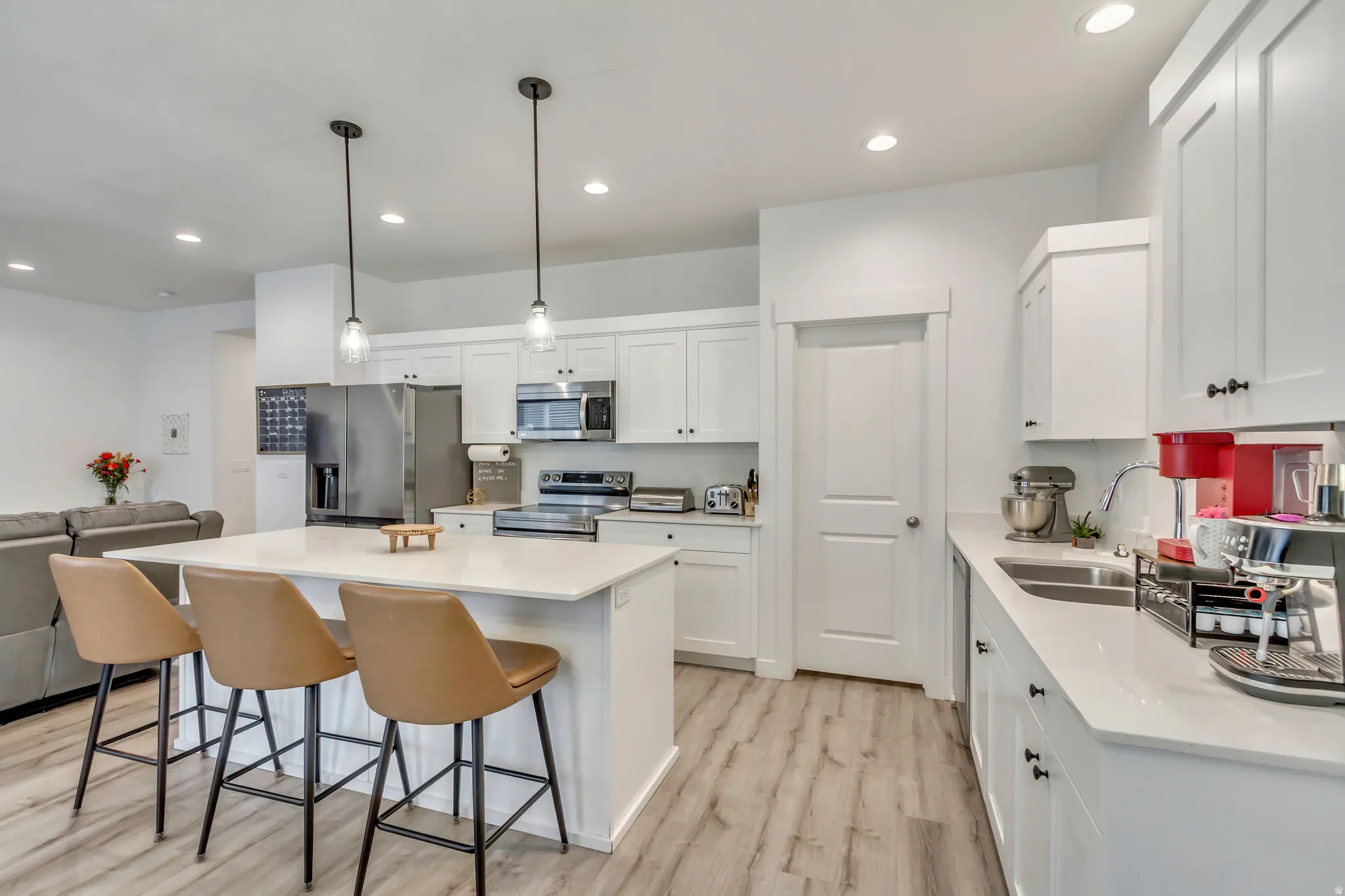 Modern kitchen featuring white shaker cabinetry, stainless steel appliances, a center island with pendant lighting, and wood-finish flooring