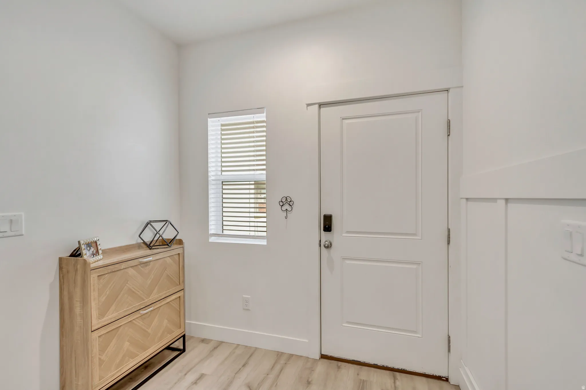 Entryway featuring a white paneled door, light wood-finish flooring, a window with blinds, and white board and batten wall detailing