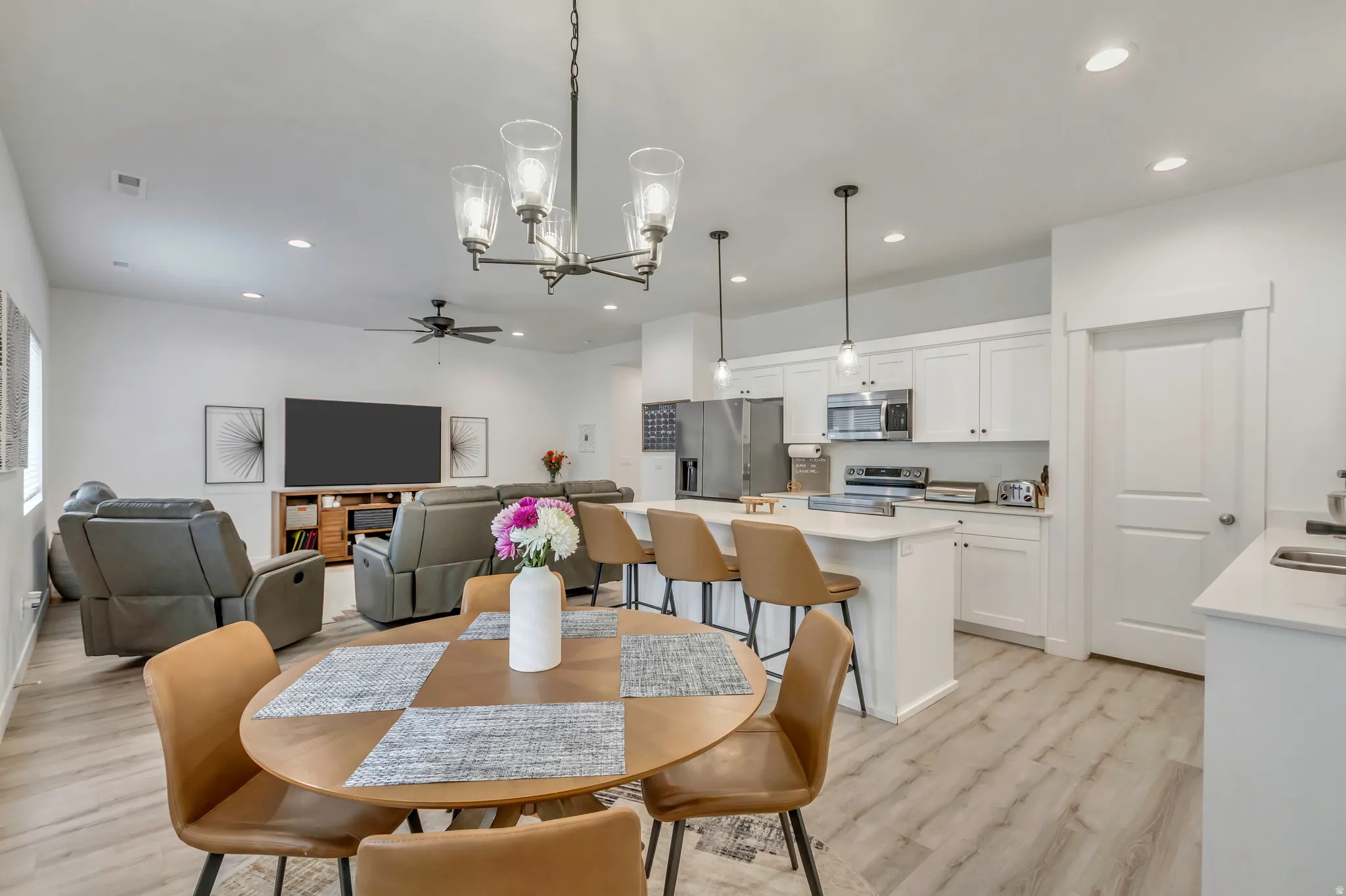 Open-concept living space featuring a dining area with a contemporary chandelier, a kitchen with white cabinetry and a central island, and a living room with recessed lighting and a ceiling fan
