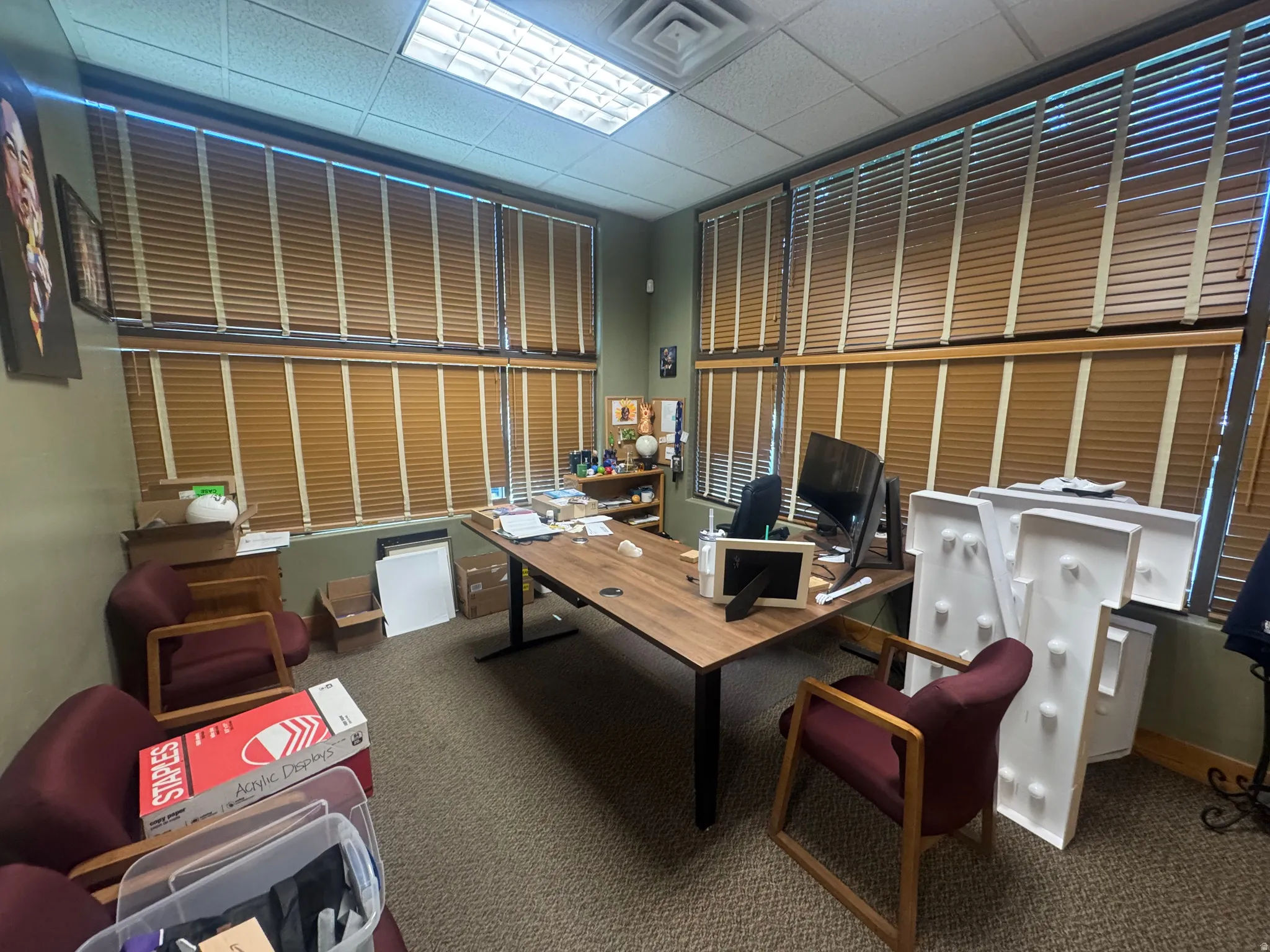 Spacious room featuring extensive window coverage with wood-tone blinds, acoustic tile ceiling with recessed lighting, and neutral carpeting