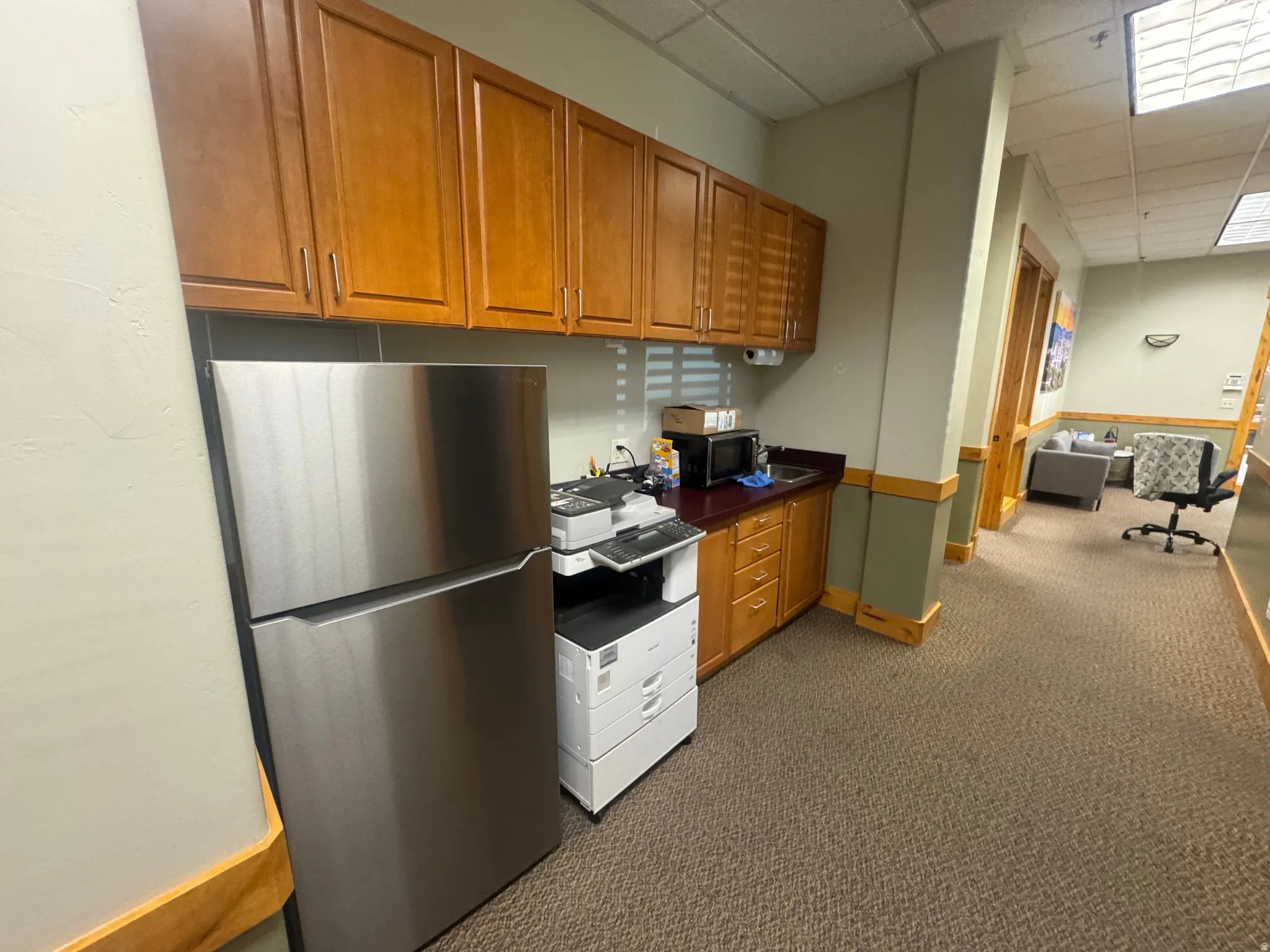 Compact kitchenette area featuring wood cabinetry, dark countertops, a stainless steel refrigerator, and recessed lighting