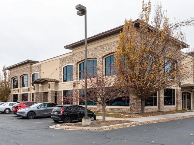 Commercial building featuring a stone and stucco exterior, arched windows, covered entryway, and asphalt parking area