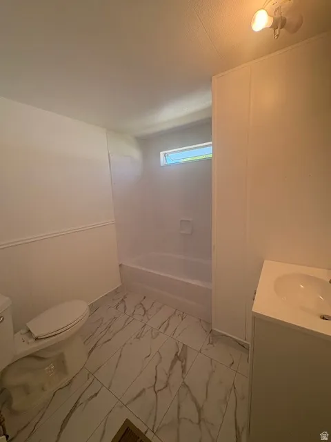 Bathroom featuring white and gray veined tile flooring, a white vanity with an integrated sink, a white toilet, and a white bathtub with a built-in soap dish
