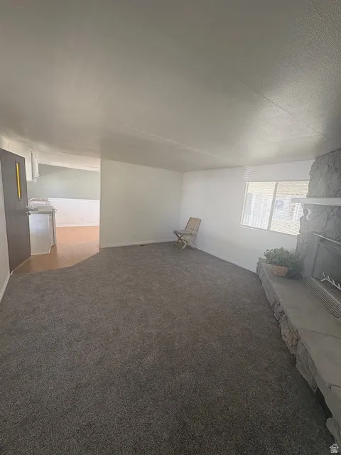 Spacious living area featuring neutral carpeting, white walls, a stone fireplace with a substantial hearth, and a large window