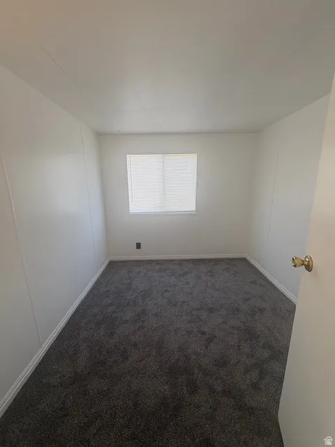 Neutral-toned room featuring a single window with blinds, dark gray carpet, white walls, and white baseboards