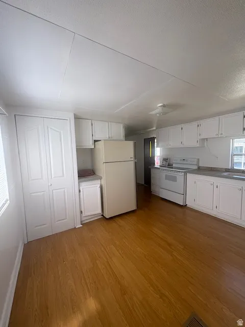 Open-concept kitchen area featuring wood-finish flooring, white cabinetry, a built-in oven range, and a built-in refrigerator