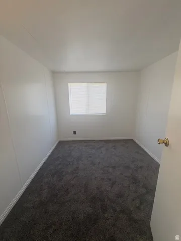 Neutral-toned room featuring a single window with blinds, dark gray carpet, white walls, and white baseboards