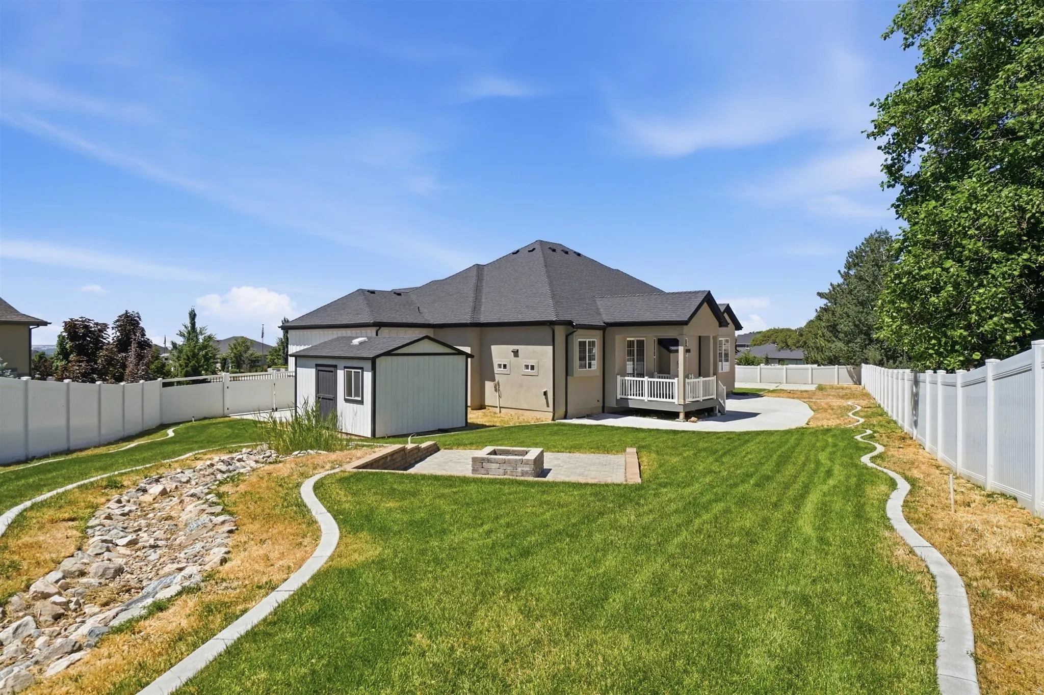 Expansive backyard with a manicured lawn, white vinyl fencing, a concrete patio, and a stone fire pit