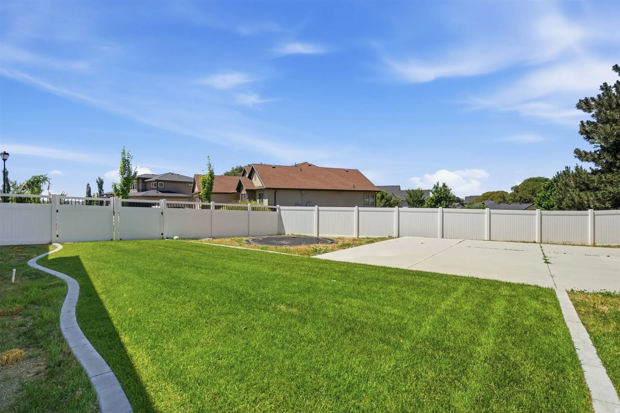 Spacious backyard featuring a manicured lawn, a large concrete pad, full perimeter fencing, a decorative concrete border, and a double gate