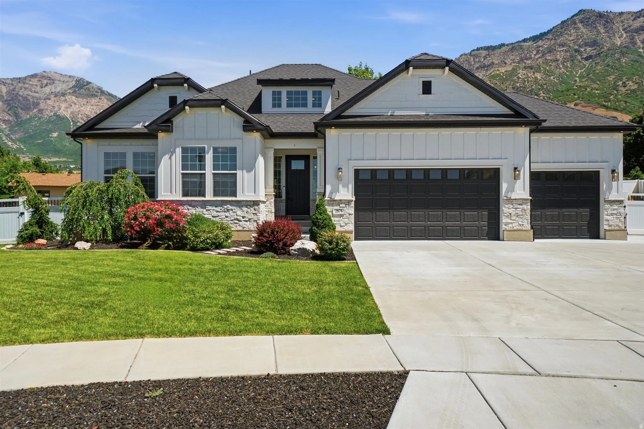 Modern farmhouse exterior with crisp white siding, dark trim, a two-car and a single-car garage, and a concrete driveway