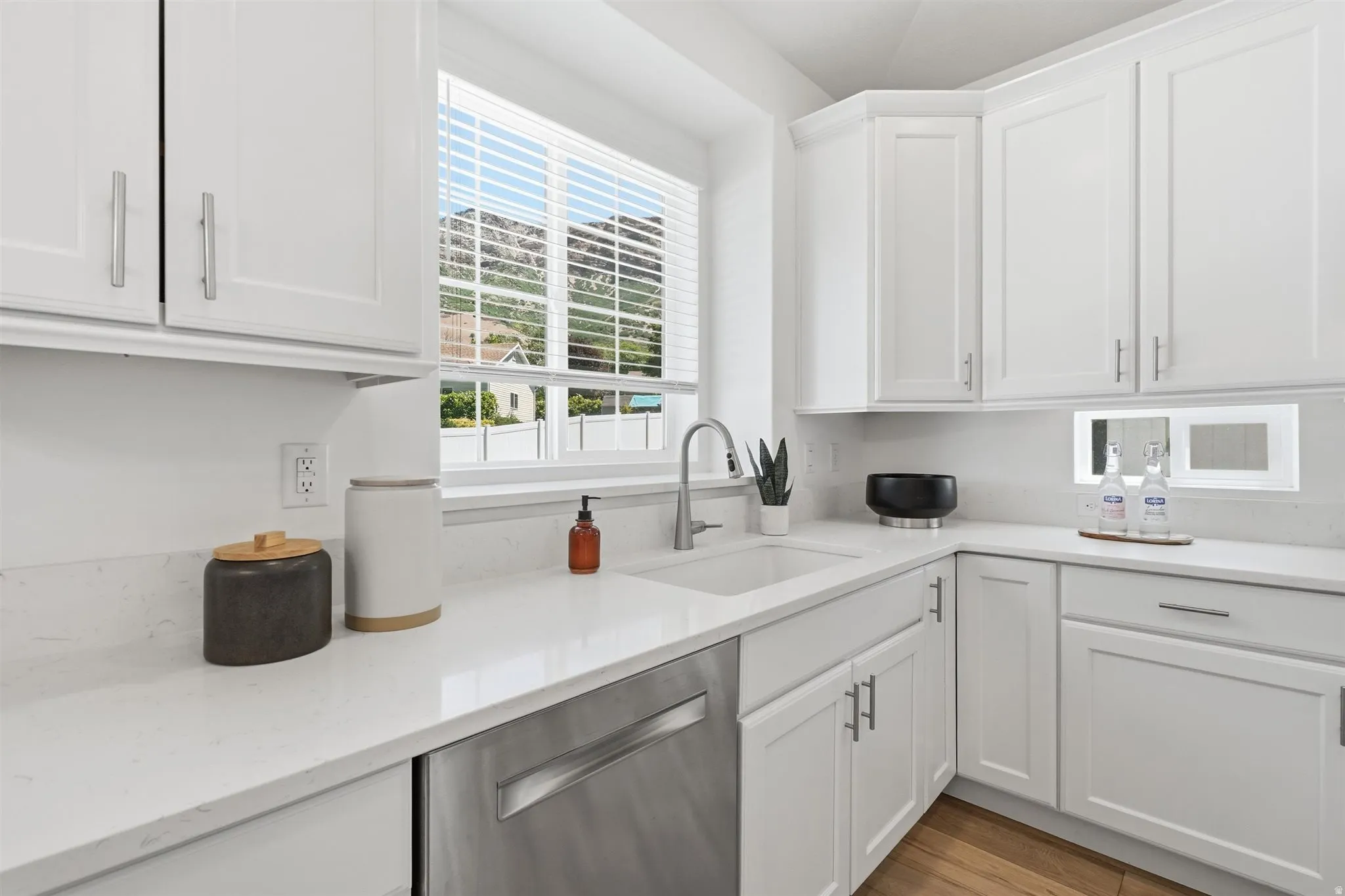 Contemporary kitchen featuring white shaker cabinetry with brushed nickel hardware, light-toned countertops, an undermount sink with a stainless steel faucet, and a stainless steel dishwasher