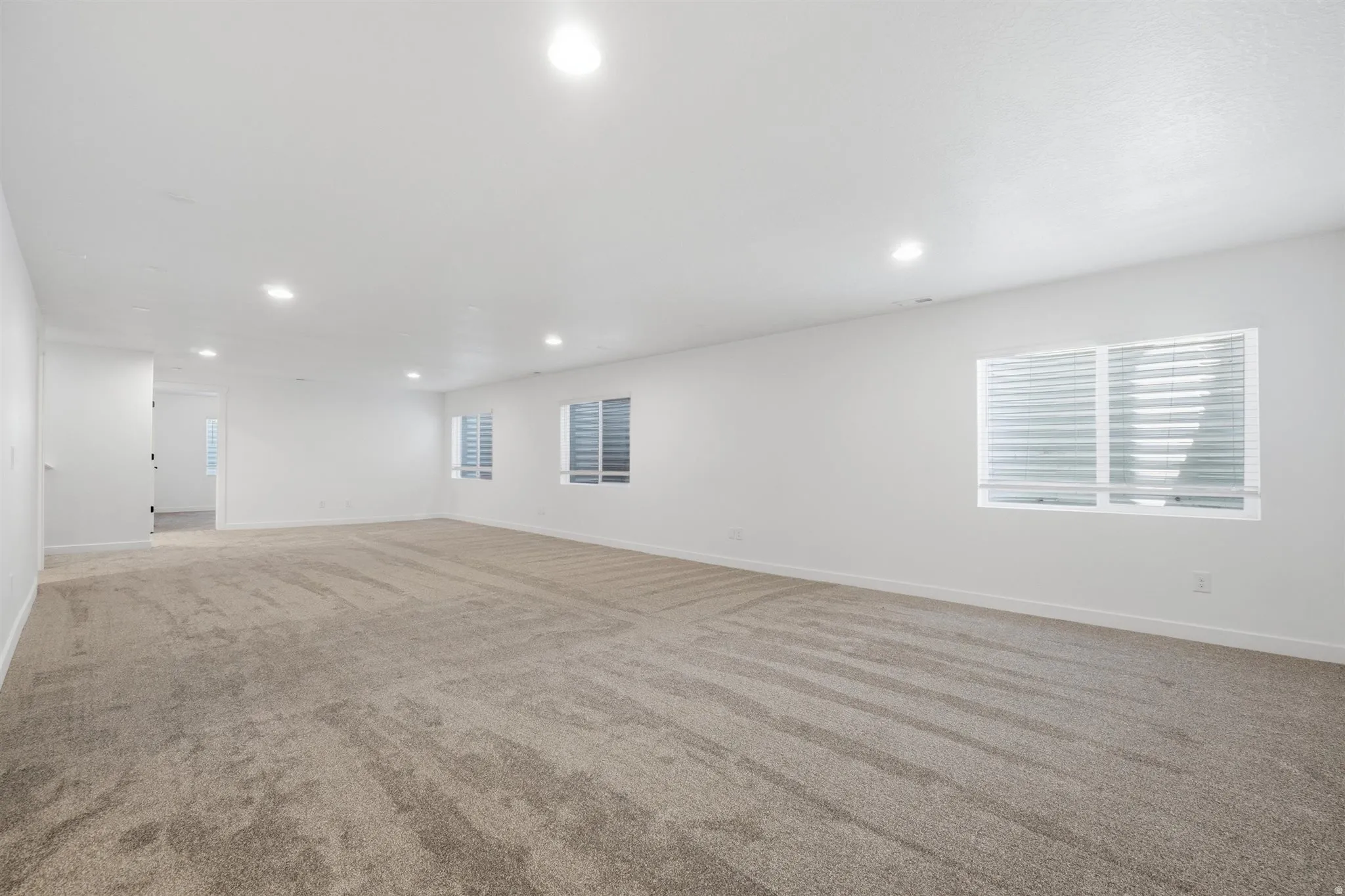 Expansive open room featuring plush carpeting, recessed lighting, and bright white walls