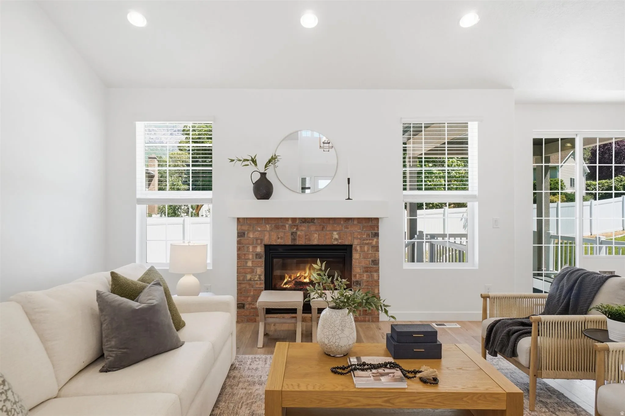 Living area featuring a brick-surround fireplace with a white mantel, recessed ceiling lighting, and wood-finish flooring
