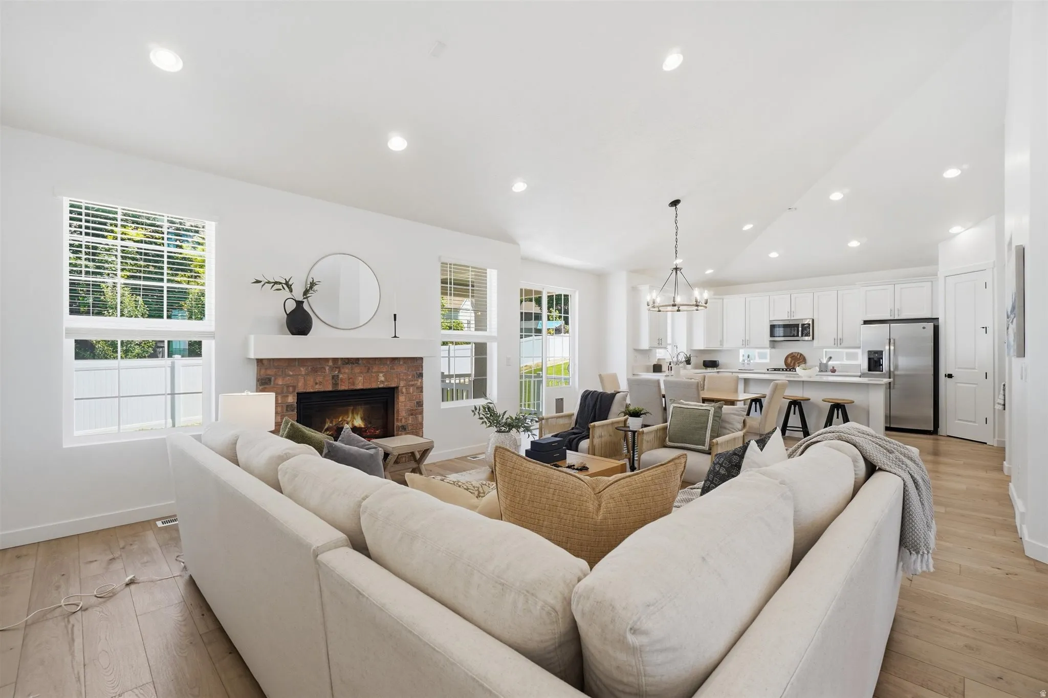 Open-concept living area featuring wood-finish flooring, a brick fireplace with a white mantel, and recessed lighting