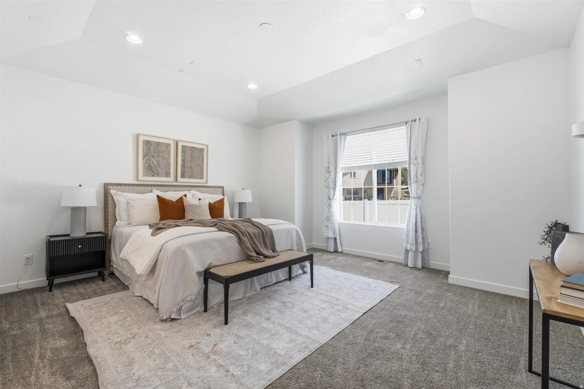 Spacious bedroom featuring light-toned carpet flooring, a large window with white blinds, recessed lighting, and a tray ceiling