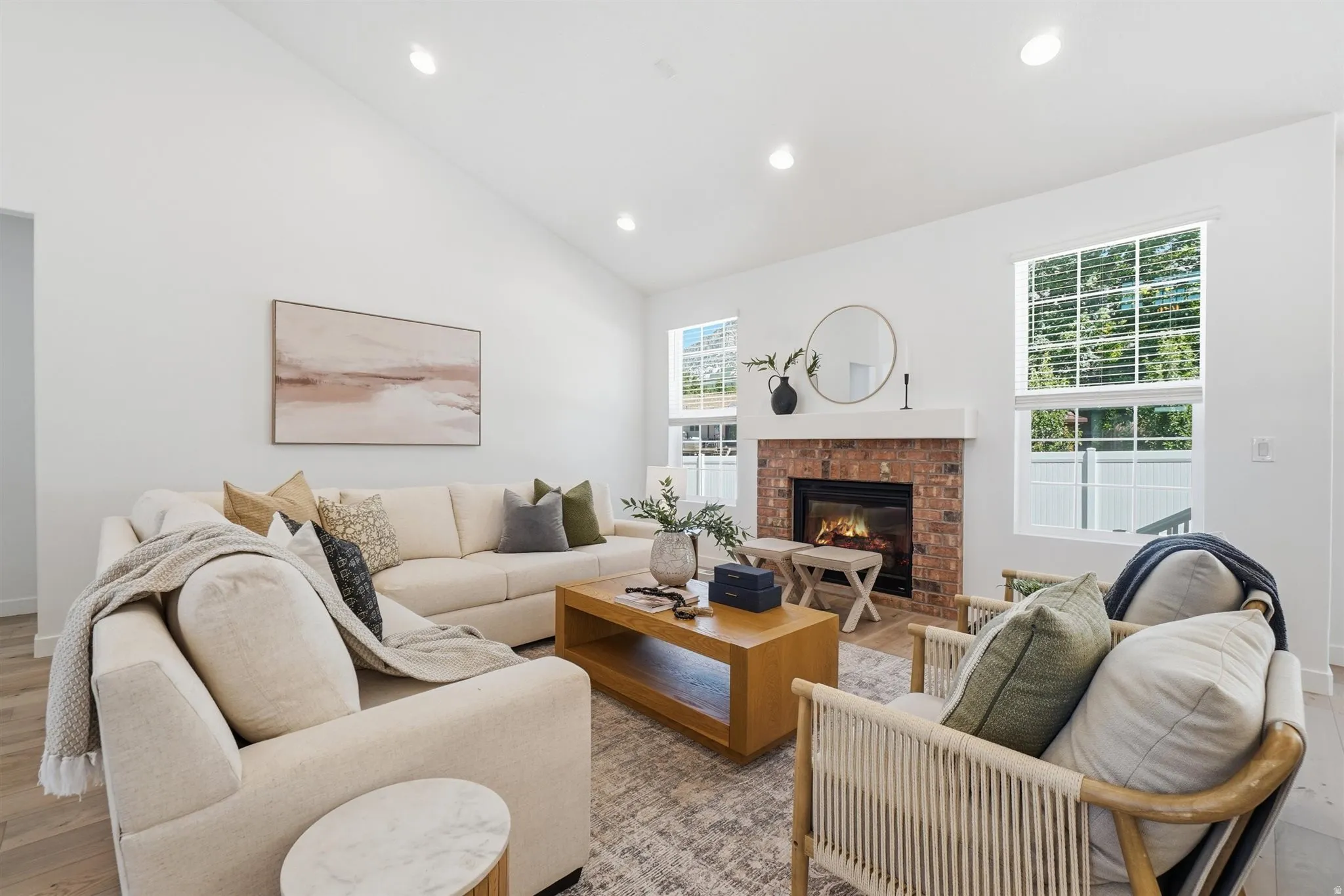 Vaulted ceiling living area featuring a brick fireplace with a white mantel, recessed lighting, wood-finish flooring, and multiple windows