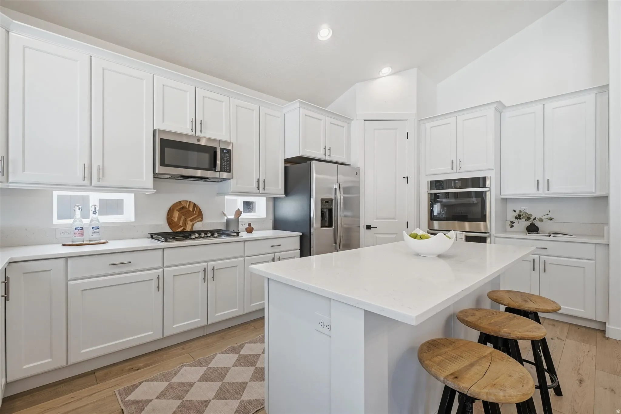 White shaker cabinetry with brushed nickel hardware, stainless steel appliances, light-toned wood-finish flooring, and a central island with a solid surface countertop