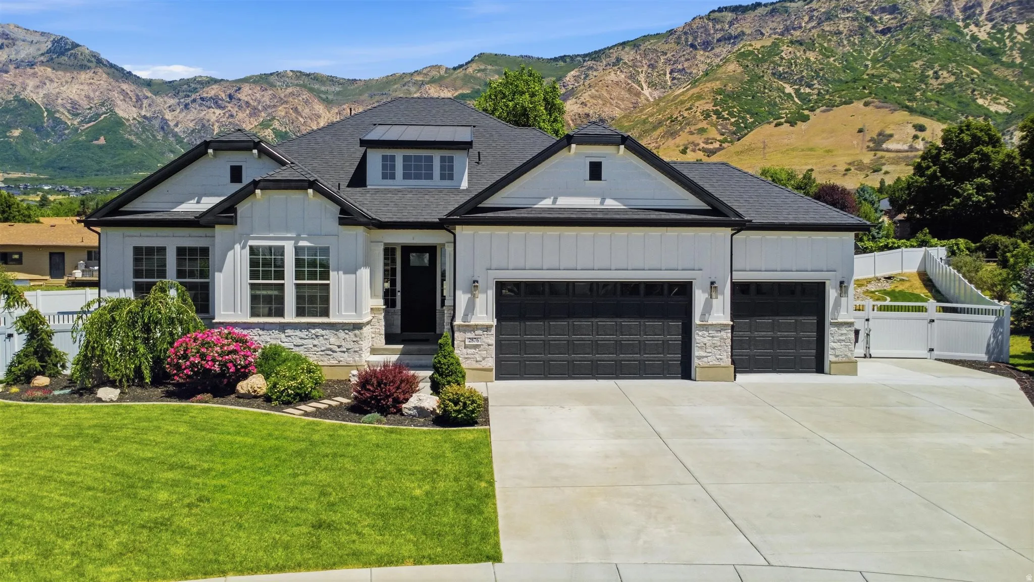 Contemporary single-story residence featuring a white board-and-batten and stone facade, dark asphalt shingle roof, and a three-car garage