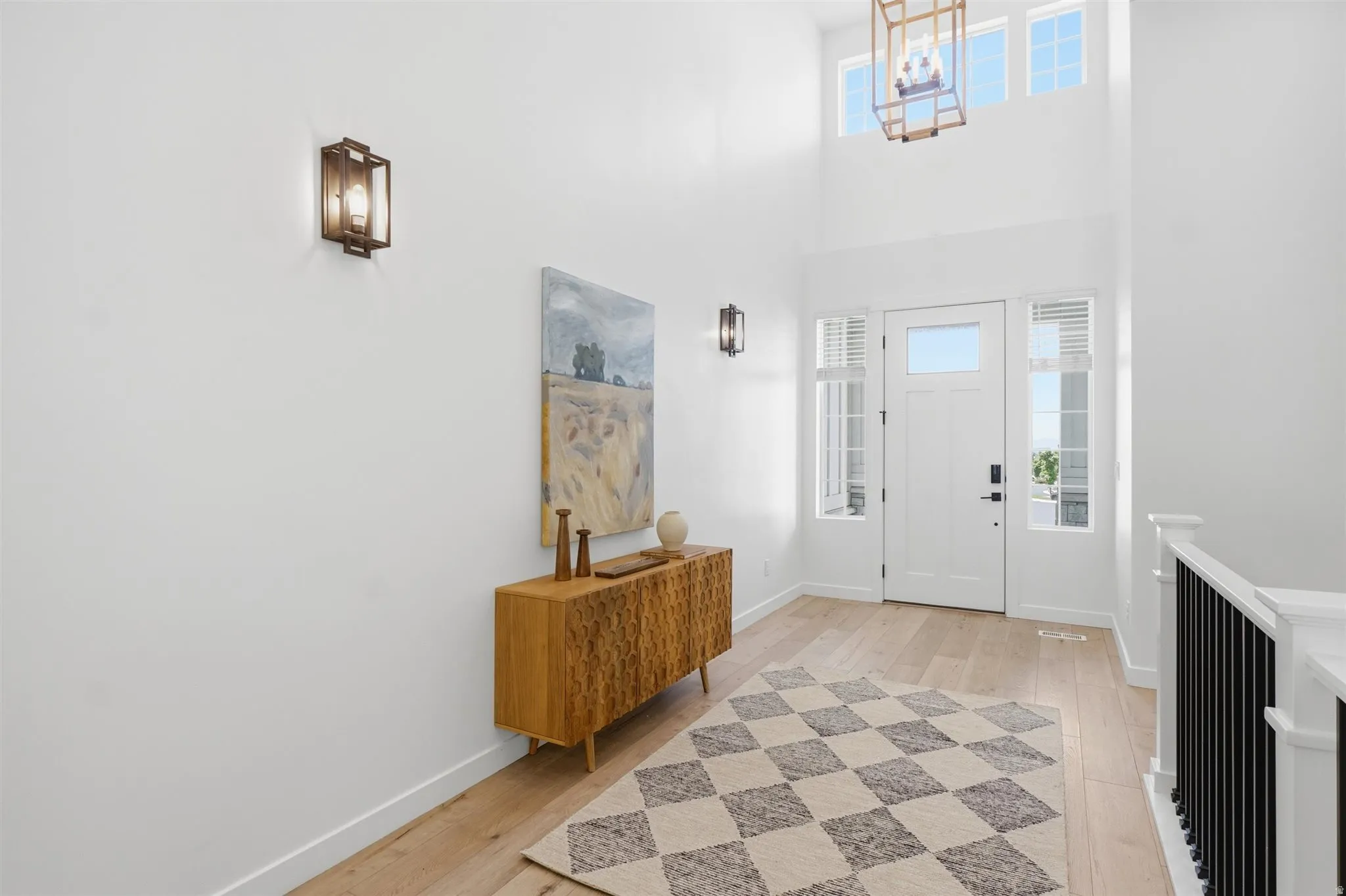 Foyer featuring high ceilings, wood-finish flooring, a white paneled entry door with sidelight windows, and a black metal spindle staircase railing