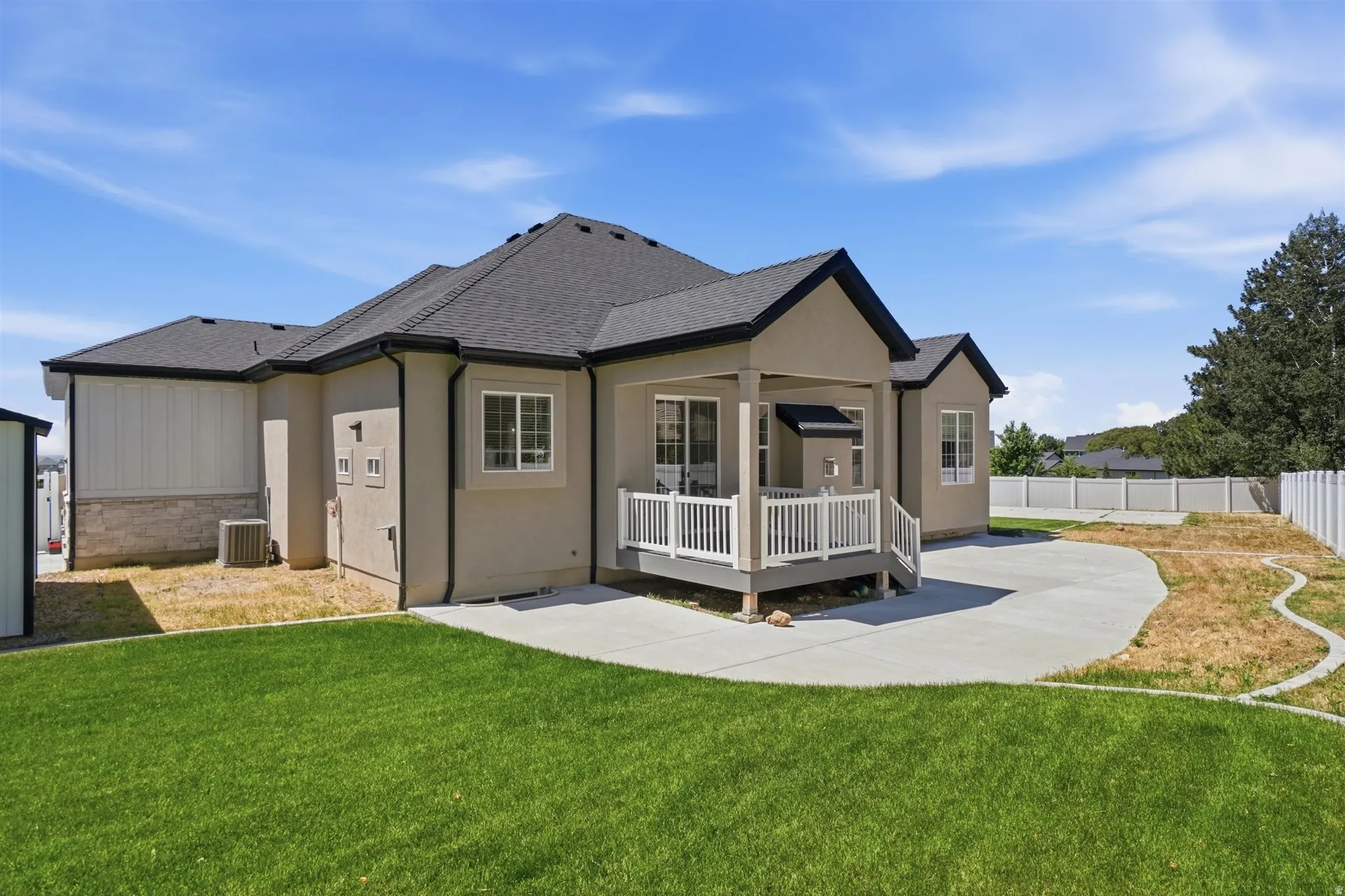 Rear exterior featuring a covered deck with white railings, a concrete patio, and a manicured lawn
