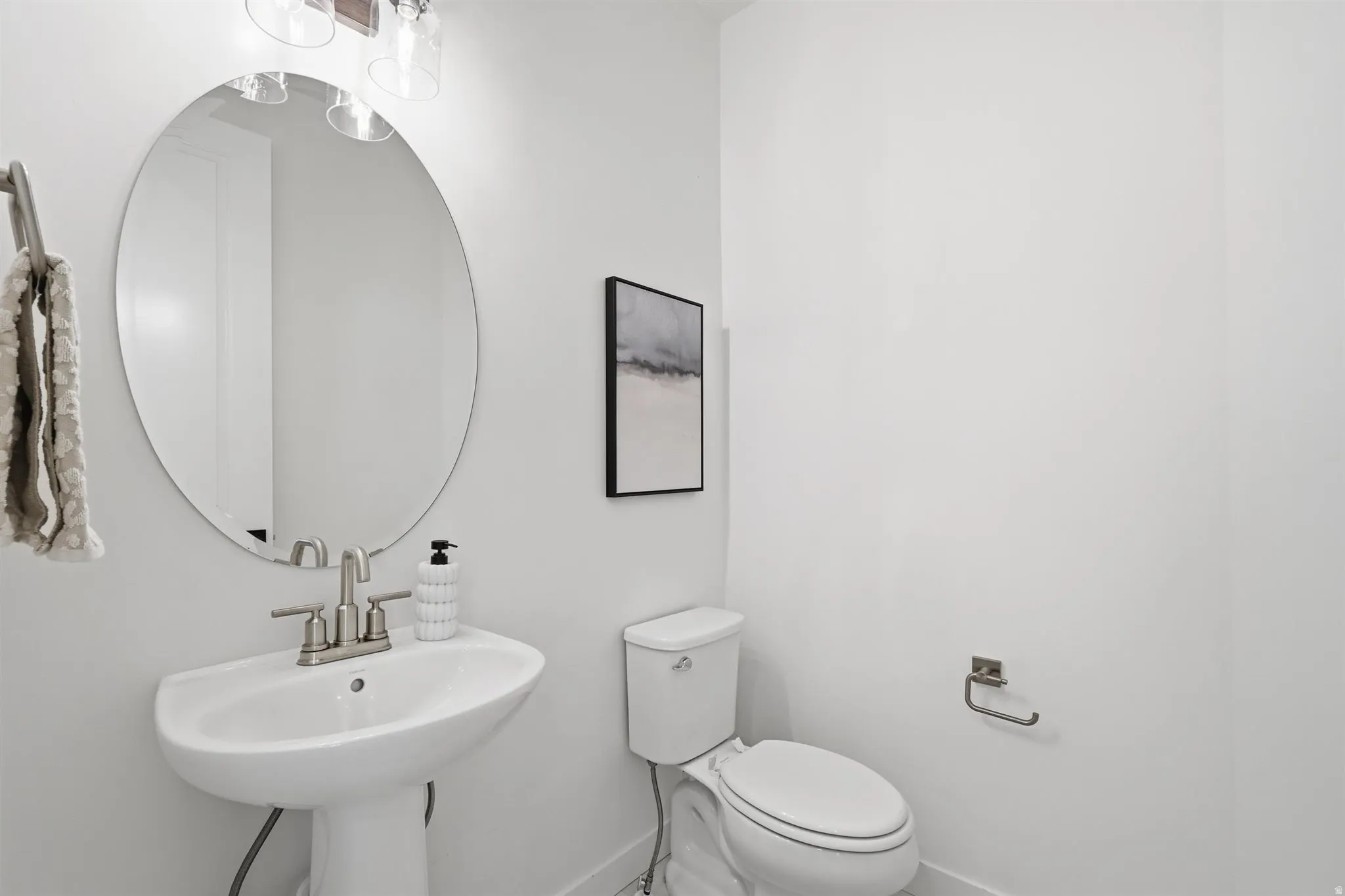 Pedestal sink with brushed nickel faucet, large round mirror, and overhead vanity lighting