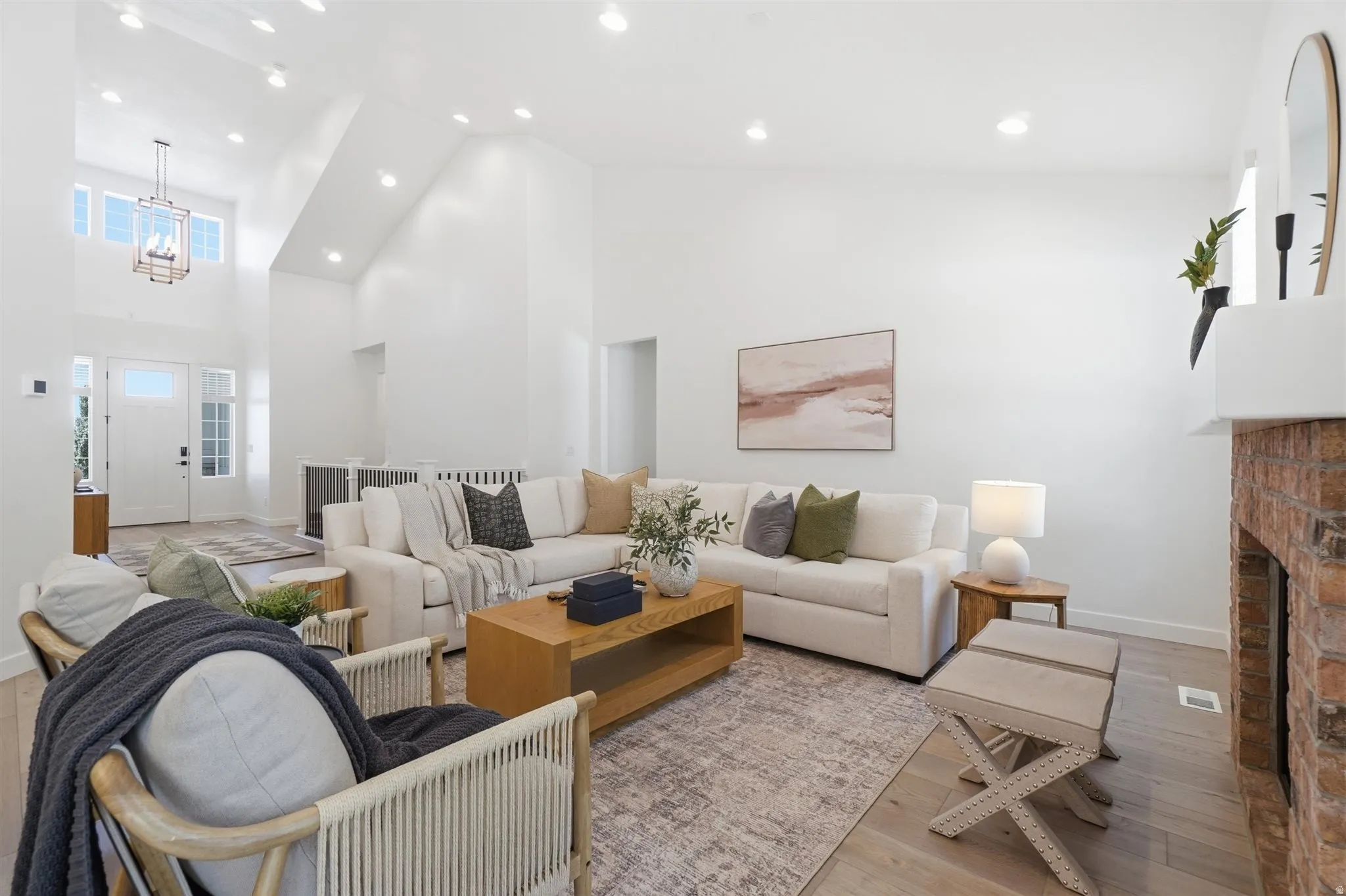 Great room featuring vaulted ceilings, recessed lighting, light wood-finish flooring, a brick fireplace with a white mantel, and a two-story entryway with a decorative chandelier