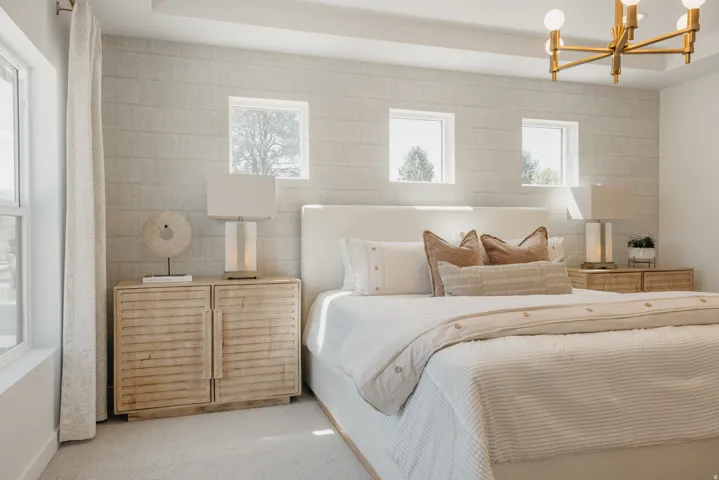 Spacious bedroom featuring textured wall treatment, recessed ceiling detail, and a modern brass chandelier