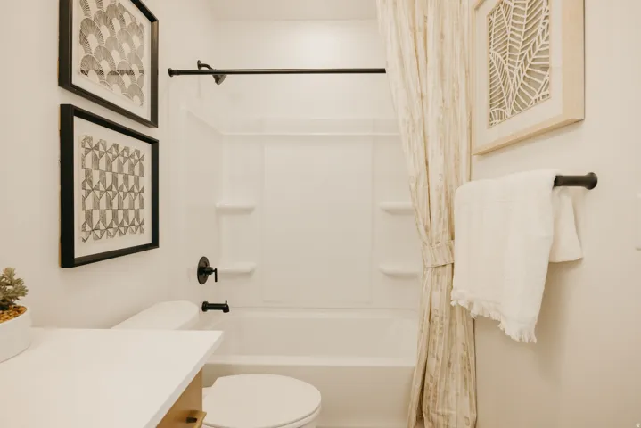 Bathroom featuring a white tub/shower combination with integrated shelving, matte black fixtures, and a white toilet