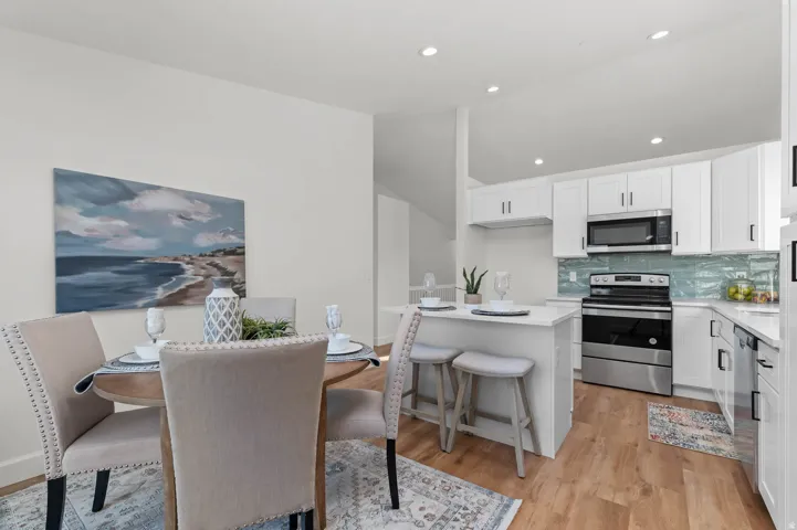 Open-concept kitchen and dining area featuring white cabinetry, stainless steel appliances, a light-toned backsplash, and recessed lighting