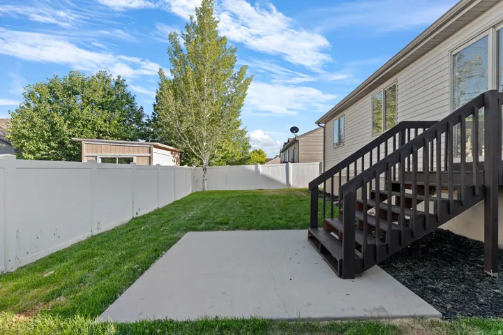 Spacious backyard featuring a concrete patio, dark wood-finish stairs, and a white vinyl fence