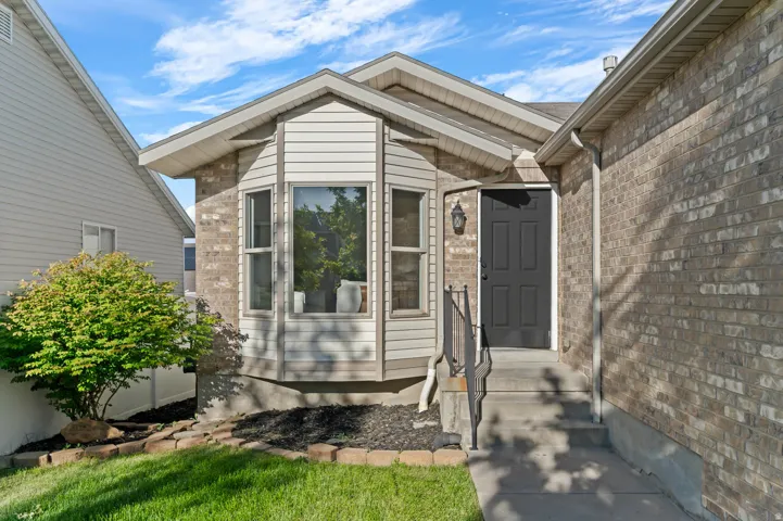 Brick and siding exterior featuring a multi-pane bay window, a dark-paneled entry door, concrete steps with a black metal handrail, and a gabled roofline