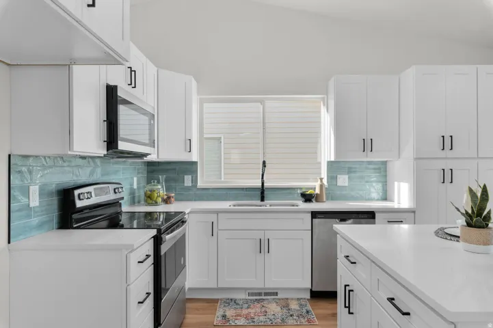 Kitchen featuring white cabinetry, a light blue subway tile backsplash, white countertops, stainless steel appliances, and wood-finish flooring